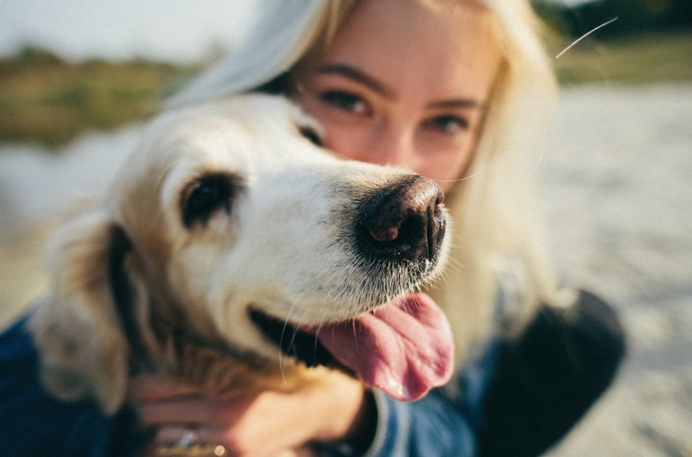 a woman with her dog in a blue jacket on the beach.
