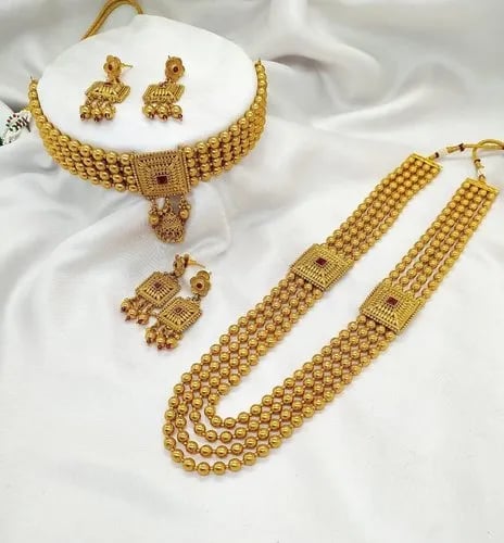 Elegant gold choker and long layered necklace set with matching earrings on white fabric.