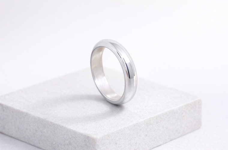 Polished 999 fine silver wedding band resting on a stone pedestal for a minimalist jewelry display.