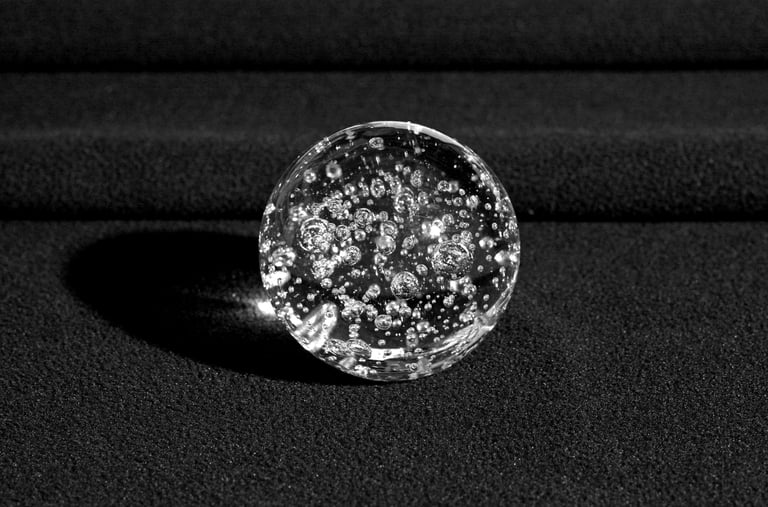 A clear glass sphere with bubbles inside, resting on a textured black surface. 