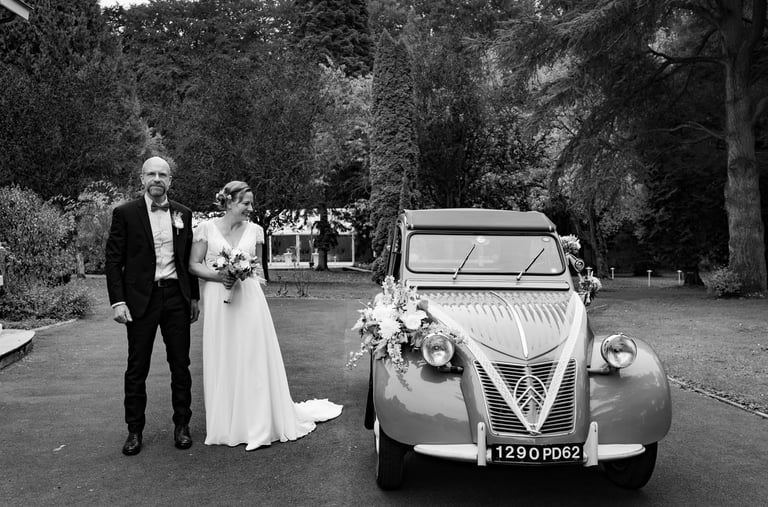 Un couple de mariés posant à côté d'une voiture ancienne