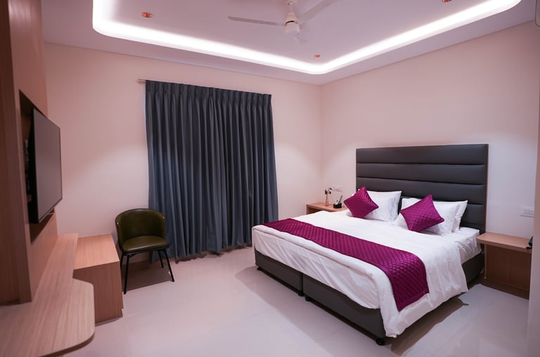 Modern hotel room with king-size bed, purple pillows, and recessed ceiling lighting.