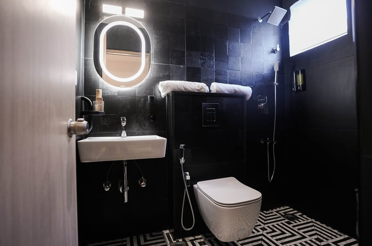 Modern luxury bathroom with black tile walls, illuminated oval mirror, and geometric floor tiles.