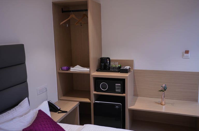Modern hotel room interior featuring a wooden open wardrobe with safe, mini fridge, and coffee station.