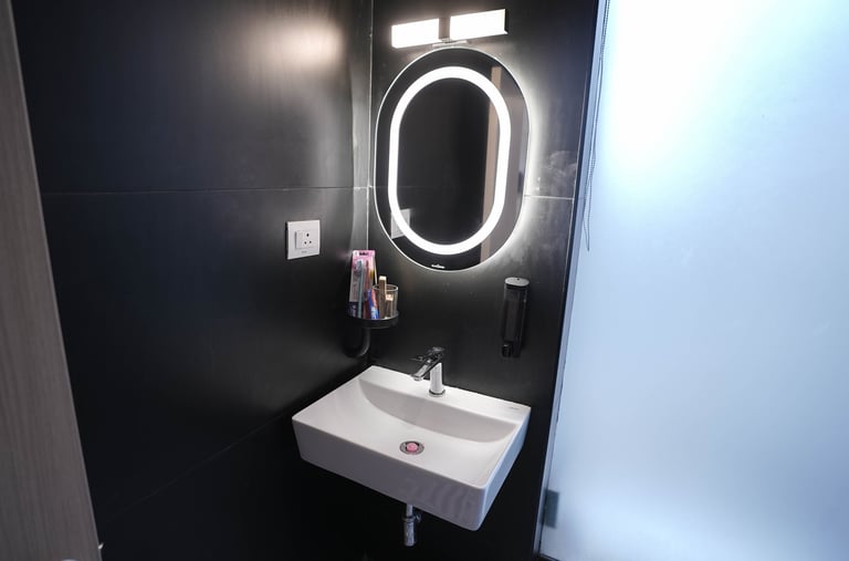 Modern bathroom featuring a white ceramic sink and an illuminated oval LED mirror against black walls.