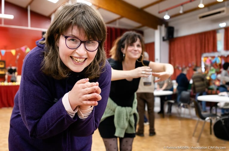 a woman in glasses and a purple sweater is smiling and holding a wii game controller