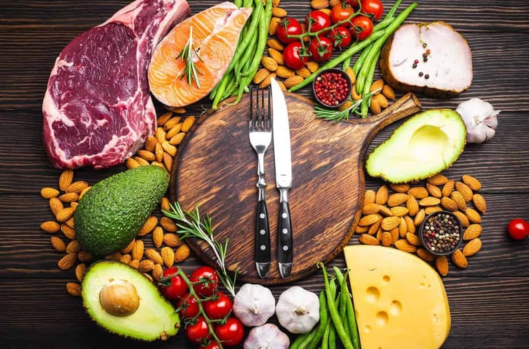  Alimentos variados como carne, peixe, queijo, abacate e vegetais em torno de tábua de madeira.
