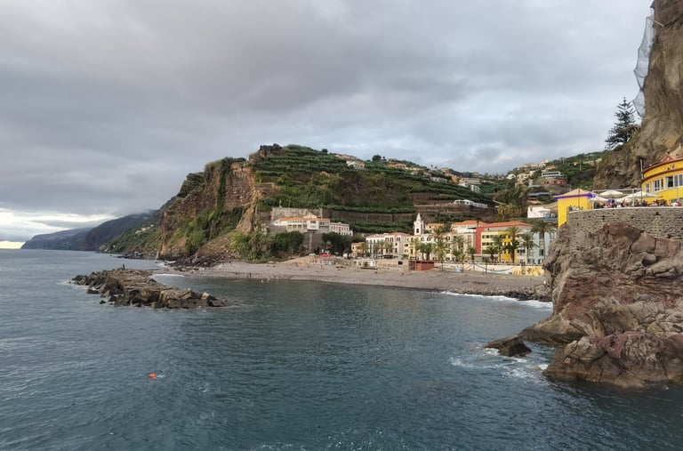 Scenic coastal view of Ponta do Sol village in Madeira with rocky cliffs and pebble beach.