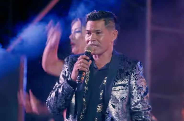 Roger Bardales in a silver paisley suit performing live on stage singing Cumbia Masha..