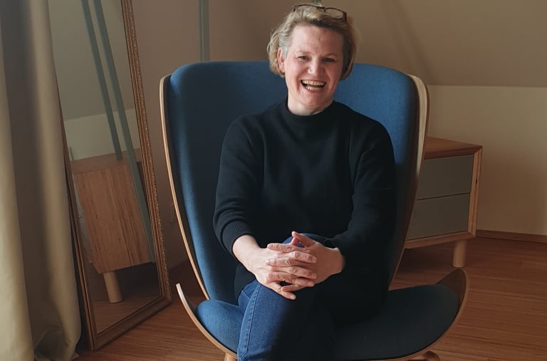 Sandra Schumacher sitzt in einem modernen blauen Ohrensessel in einem lichtdurchfluteten Raum.