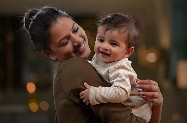 A happy mother holding her smiling baby boy in a warm, indoor setting.
