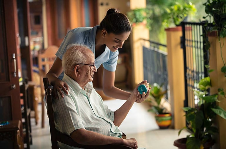 A young caregiver assisting a senior man with light weightlifting exercises for geriatric physical therapy.