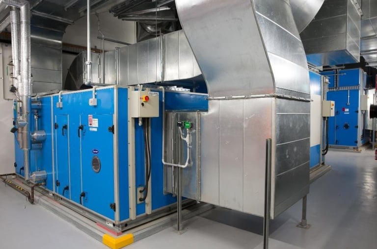 Industrial blue HVAC air handling unit with galvanized steel ductwork in a mechanical plant room.