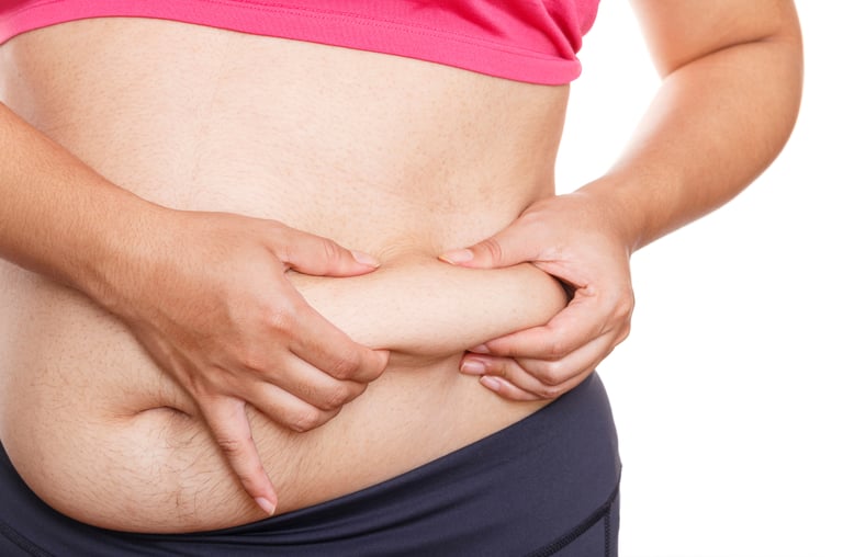 A woman pinching excess belly fat on her stomach to show weight gain or weight loss progress.