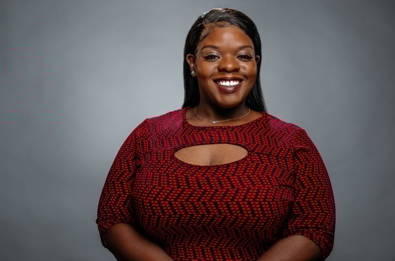 Close-up professional portrait of Clarice Corinn smiling confidently in a red patterned dress.