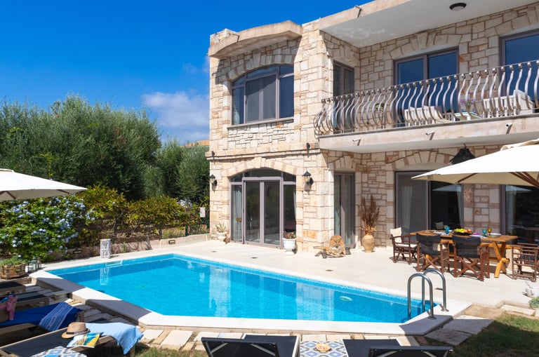 a pool with sunbeds and umbrellas in front of a holiday villa