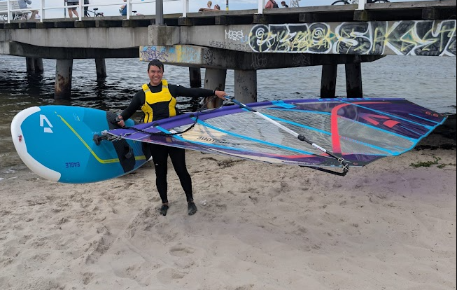 Lennard holding a colorful windsurf board on the beach before heading into the water