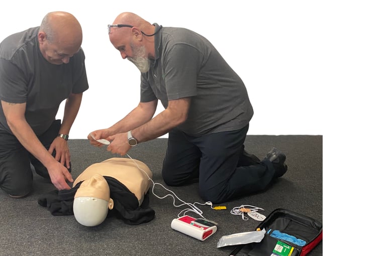 2 men knelt over a training adult manikin, the manikins shirt is raised, AED pads are being attached