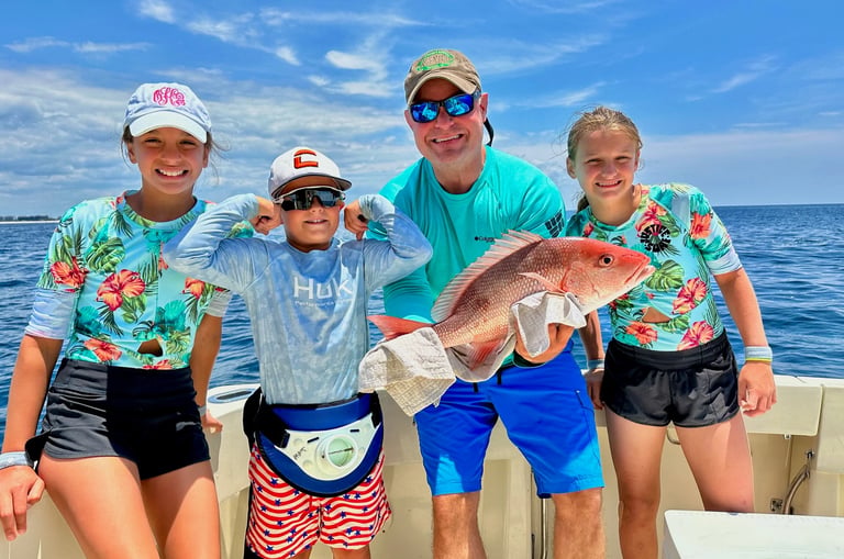 A happy family on a deep sea fishing charter holding a large red snapper caught in the ocean.
