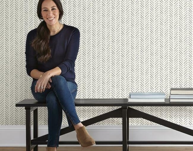 Joanna Gaines sits on a black bench against black and white herringbone peel and stick wallpaper.
