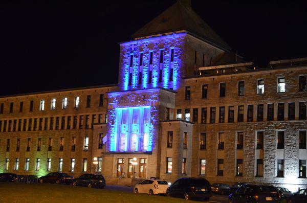 Historic stone government building illuminated with bright blue lights at night.