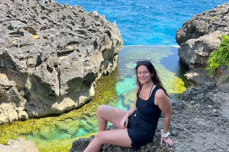 A woman sits on volcanic rocks by the turquoise waters of Angel's Billabong in Nusa Penida, Bali.