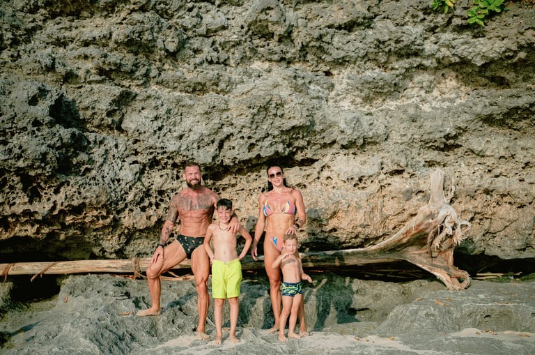 Family standing beneath a coastal cliff during a beach family photography session at Dreamland Beach Bali.