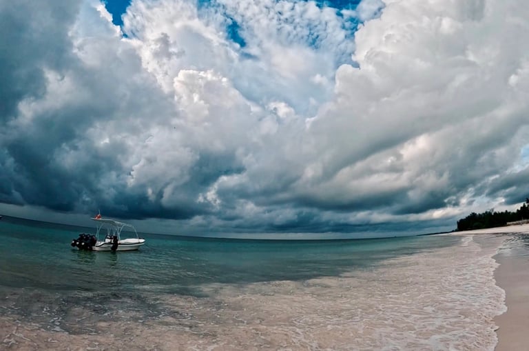 A small motorboat anchored near a tropical beach under dramatic storm clouds and a blue sky.