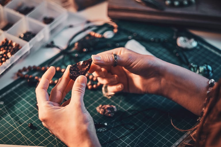 Manos de un joyero inspeccionando una piedra preciosa oscura en un banco de trabajo.