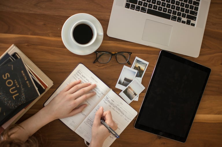 Une personne écrit sur un cahier sur une table avec un ordinateur portable à côté