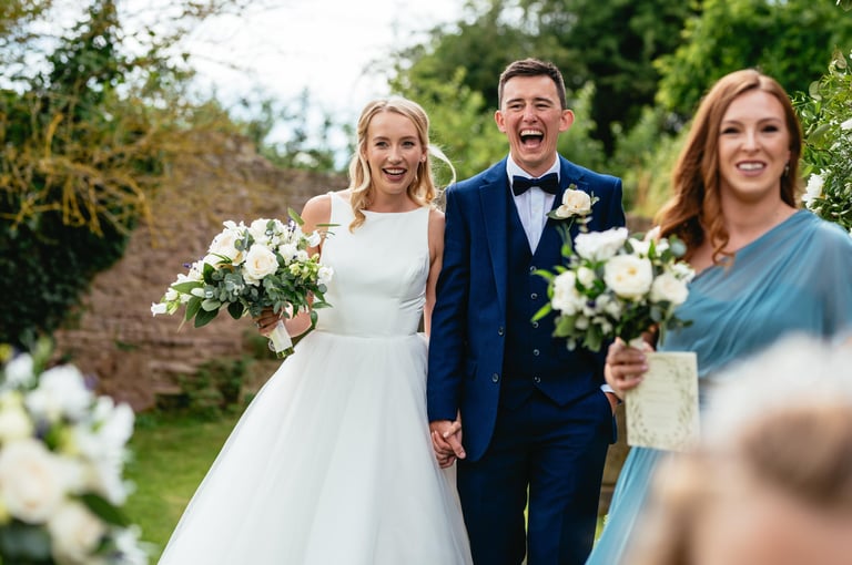 Bride and groom laugh as they walk hand in hand at a South Wales countryside wedding, captured by photographer Owen Mathias