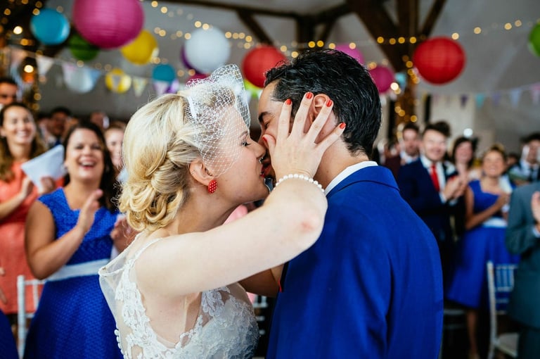a bride in vintage dress and groom in blue suit kissing at a wedding ceremony