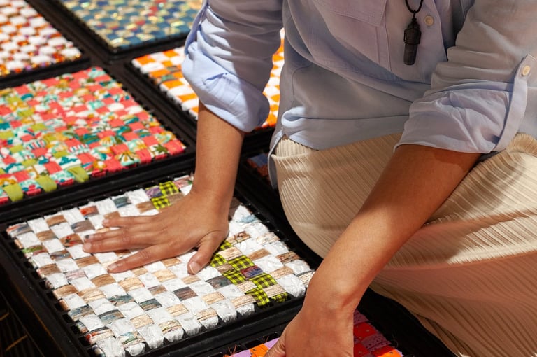 Woman on milk crates touching colorful Punjabi textiles arranged around her.