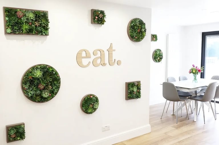 Modern dining room featuring framed succulent wall art and an 'eat' sign next to a white table.