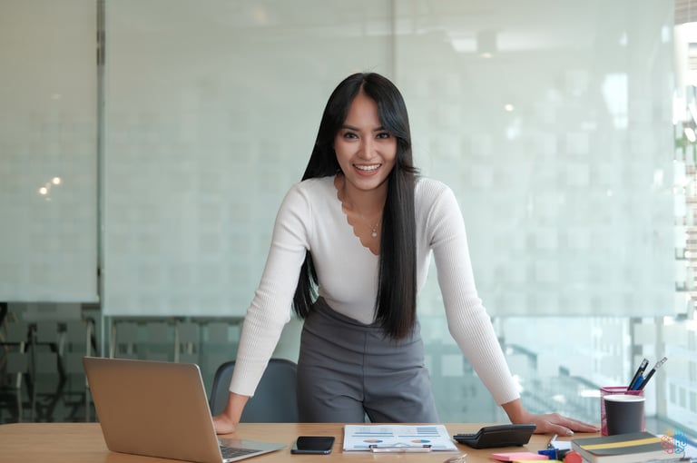 Curso de Assistente Contábil: Imagem de uma mulher sorrindo apoiada em uma mesa de escritório