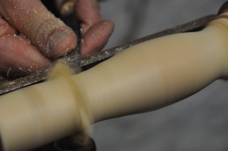 A close-up of a hand holding a chisel, turning wood spinning on a lathe