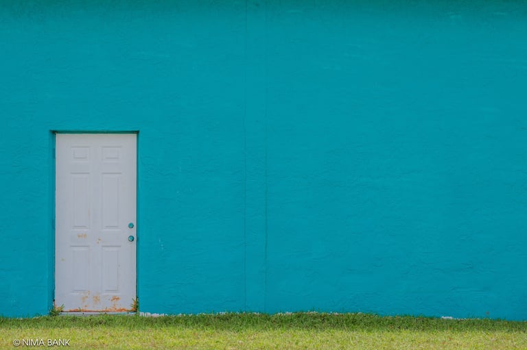 a white rusty door against a teal blue building