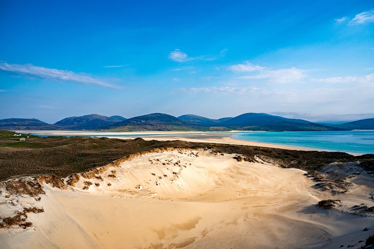 La plage de Luskentyre dévoile ses vastes dunes de sable doré, bordée par une mer turquoise et des montagnes lointaines.