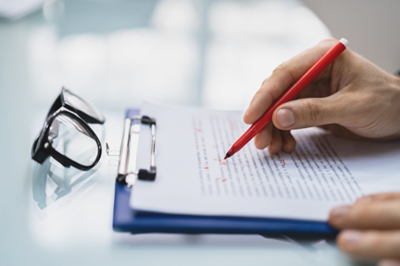 A person holding a pen and writing on a paper representing editing and proofreading