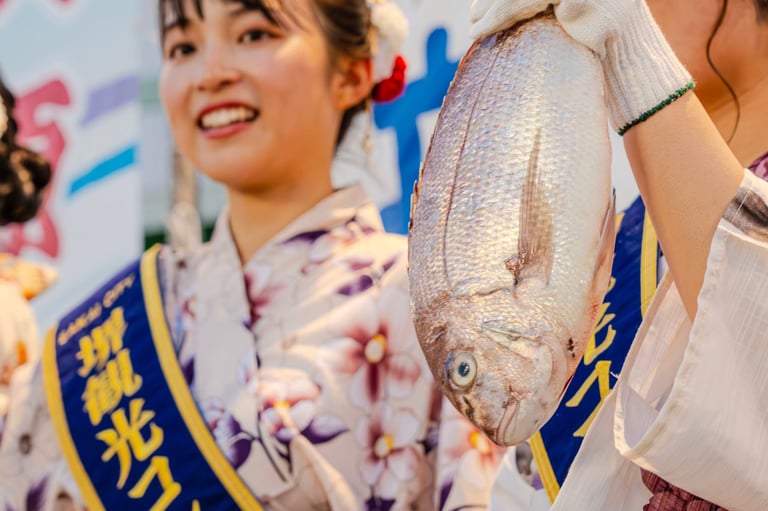 浴衣姿の女性が堺観光コンパニオンのタスキを掛け、魚セリで大きな鯛を掲げているニュース写真。