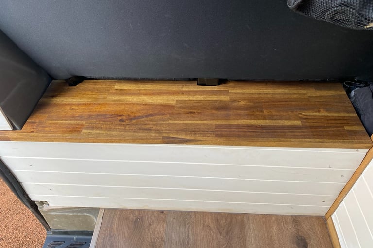 Custom camper van interior featuring a wooden butcher block bench seat and white shiplap paneling.