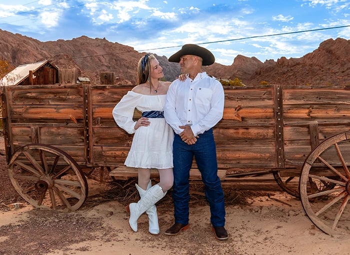 a man and woman in cowboy attire standing in front of a wagon