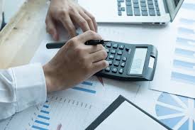 Accountant using a black calculator and pen to analyze financial data reports and charts.