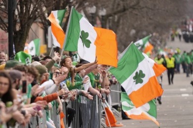 Crowds waving Irish flags with shamrocks at a St. Patrick's Day parade event.