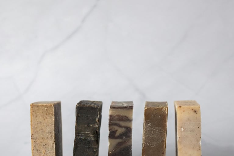 A row of five assorted natural handmade soap bars standing upright on a white marble surface.