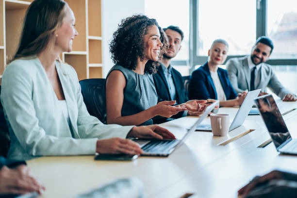 a group of business people sitting at a table with laptops