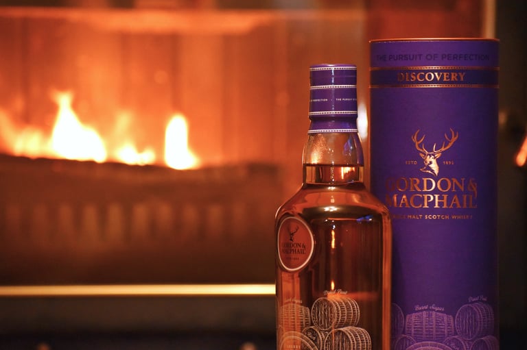 A bottle and cask of Gordon & Macphail single malt scotch whisky in front of a fireplace