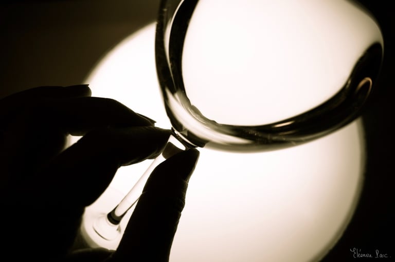 Vue en gros plan d’un verre de vin de profil, avec des doigt qui tiennent le pied du verre.