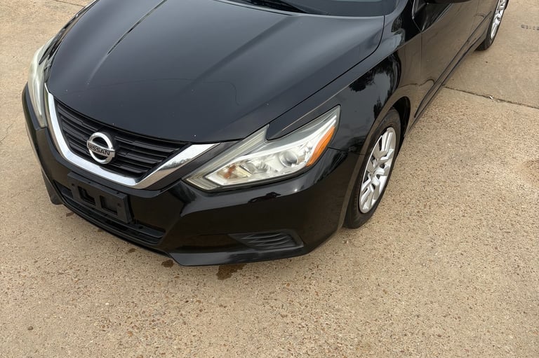 A black Nissan Altima sedan parked on a concrete lot at a used car dealership.