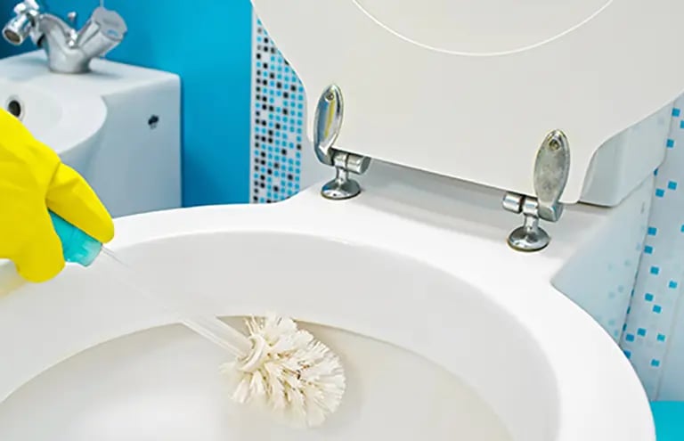 a person cleaning a toilet with a yellow glove
